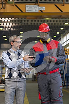 Manager Giving Orders To Black Worker in Protective Workwear With Clipboard