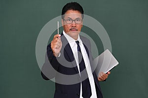 A manager in his smart suit holding laptop on left hand and pointing his pen on his right hand