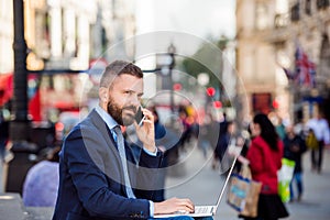 Manager with laptop and smart phone, sunny Piccadilly Circus, Lo