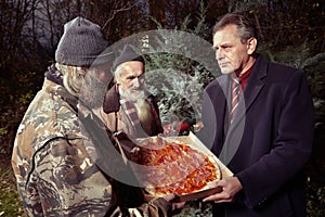 Man in suit giving pizza to two homeless men in park photo