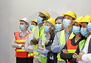 Manager and the rest of the engineering team standing together in the factory wearing facial mask during new normal