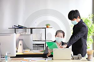 Manager and secretary are working in business office while wearing medical face mask for