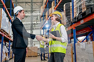 Manager shake hands with warehouse factory worker woman who hold tablet and express happiness with smiling and they stay in front