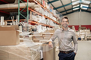 Manager smiling while leaning against stock in a large warehouse