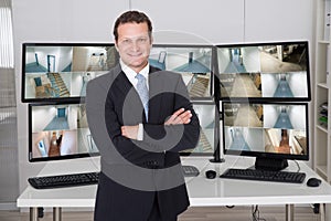 Manager Standing Arms Crossed Against Monitors At Office