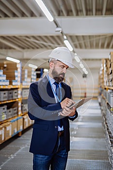 Manager in suit controlling goods in a waehouse.