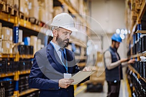 Manager in suit controlling goods in a warehouse.