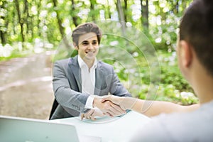 Manager in suit welcomes with handshake at interview new worker man at his office table in green park forest. Business concept.