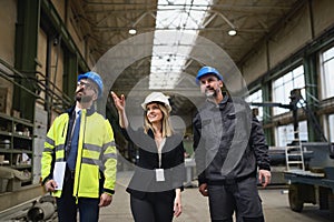 Manager supervisors and industrial worker in uniform walking in large metal factory hall and talking.