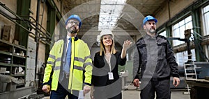 Manager supervisors and industrial worker in uniform walking in large metal factory hall and talking. Low angle view.