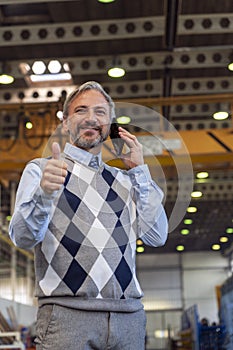 Manager Talking On Smartphone, Looking At Camera And Giving Thumb Up In A Factory