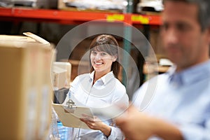 Manager In Warehouse With Worker Scanning Box In Foreground