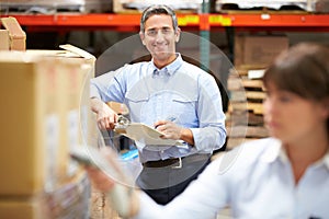 Manager In Warehouse With Worker Scanning Box In Foreground