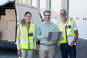 Manager and warehouse workers standing with laptop and clipboard