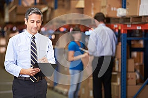 Manager In Warehouse Writing On Clipboard