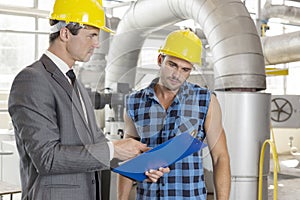 Manager with worker discussing over clipboard in industry