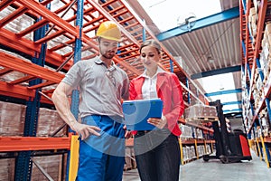 Manager and worker in high bay warehouse discussing business