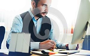 Manager writes in notebook at home workplace. Bearded businessman working at office. Consultant thinking looking in monitor