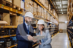 Managers in suit controlling goods in a waehouse.