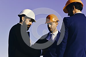 Managers wear smart suits, ties and hardhats on blue sky background. Constructors hold clip folder. Building and