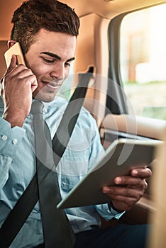 Managing business on the go. Shot of a young businessman talking on a phone while using a digital tablet in the back