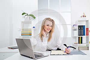 Managing Business Work. Happy young business woman using pc at office. Gorgeous blond secretary woman writing down notes