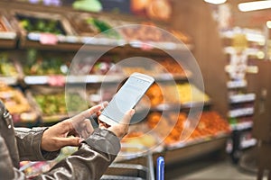 Managing her shopping with a mobile app. a woman using a mobile phone in a grocery store.