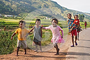 Manandoana, Madagascar - April 26, 2019: Group of unknown Malagasy kids running on road next to rice field, small hills in