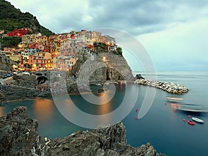 Manarola in the evening, illuminated by lampposts and by the light of the sunset with a cloud in the sky