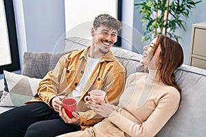 Mand and woman couple drinking coffee sitting on sofa at home