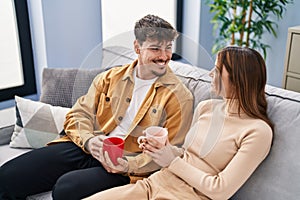 Mand and woman couple drinking coffee sitting on sofa at home