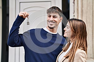 Mand and woman couple hugging each other holding key of new home at street