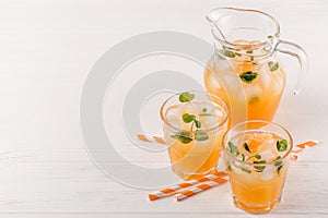 Mandarin cocktail with ice and mint in beautiful glasses and jug, fresh ripe citrus on white wooden background. Sweet orange juice