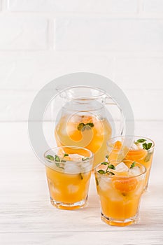 Mandarin cocktail with ice and mint in beautiful glasses and jug, fresh ripe citrus on white wooden background. Sweet orange juice