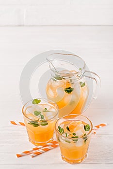 Mandarin cocktail with ice and mint in beautiful glasses and jug, fresh ripe citrus on white wooden background. Sweet orange juice