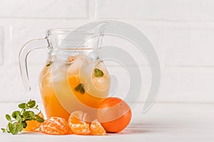 Mandarin cocktail with ice and mint in beautiful glasses and jug, fresh ripe citrus on white wooden background. Sweet orange juice