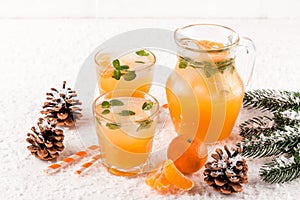 Mandarin cocktail with ice and mint in beautiful glasses and jug, fresh ripe citrus on white wooden background. Sweet orange juice