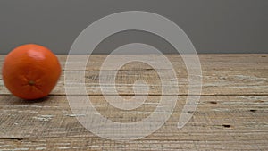 A mandarin rolls and stops on a wooden surface on a gray background.