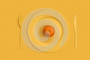 Mandarin on top on a yellow plate, knife and fork. On a yellow background. View from above.