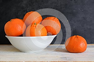 Mandarine and clementine next to a bowl on a white wooden table.