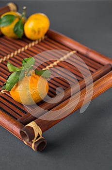 Mandarine fruite with leaves on a bamboo tray on a grey background