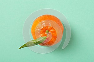 Mandarine with leaf on a mint green background, top view, minimalist style