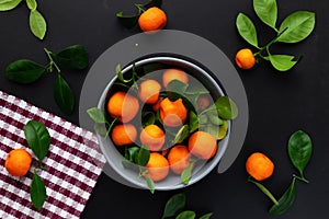 Mandarins or clementines with leaves on a black background. Tangerines in a plate Top view.