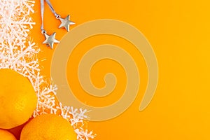 Mandarins, silver toy stars and snowflakes on a orange background. Winter Holiday festive greeting card with copy space for the