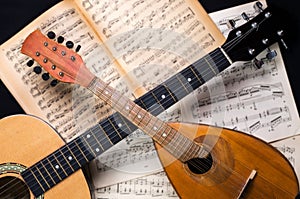 Mandolin and guitar with blurred sheet music books on a black background.