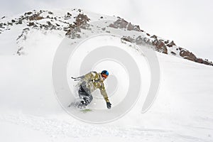 Manful snowboarder riding down the slope in the mountain resort