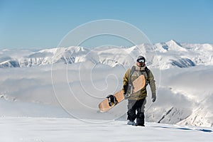 Manful snowboarder walking with the brown snowboard in the mount photo