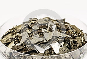 Manganese samples in petri dish, pure manganese metal flakes used in industry, isolated white background , macro photography