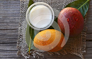 Mango body butter in a glass bowl and fresh ripe mangoes fruit on old wooden table.