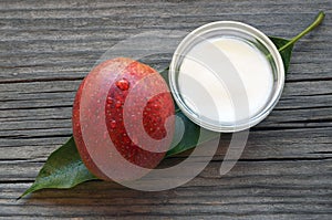 Mango body butter in a glass bowl and fresh ripe organic mango fruit and leaf on old wooden background.